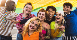 Seven friends smiling and holding a rainbow flag